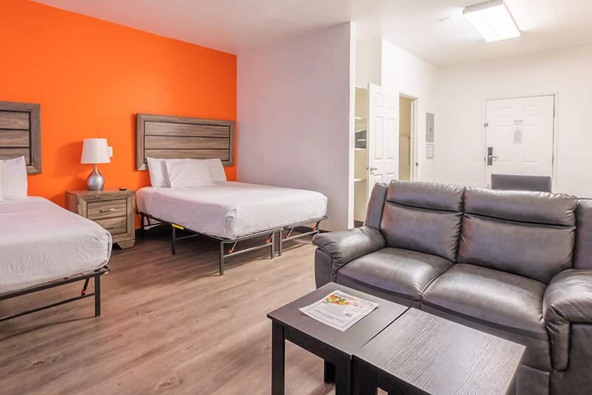 A hotel room with two beds, a sofa, a table, and a bright orange wall.