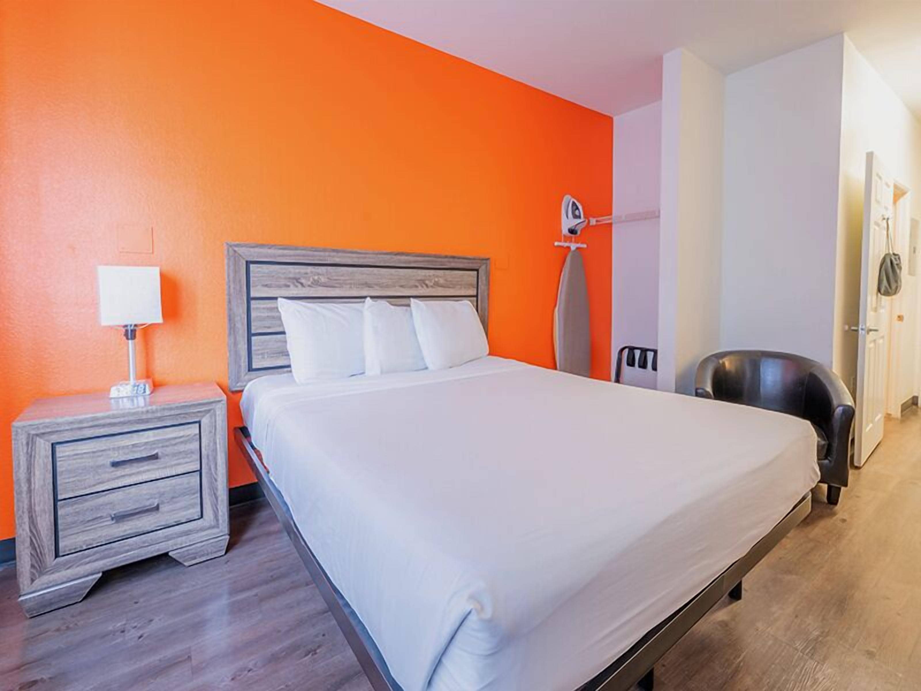 Una habitación de hotel con una cama, una mesita de noche, una silla y un tablero para planchar.