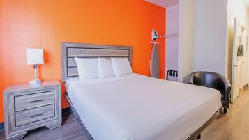 Una habitación de hotel con una cama, una mesita de noche, una silla y un tablero para planchar.