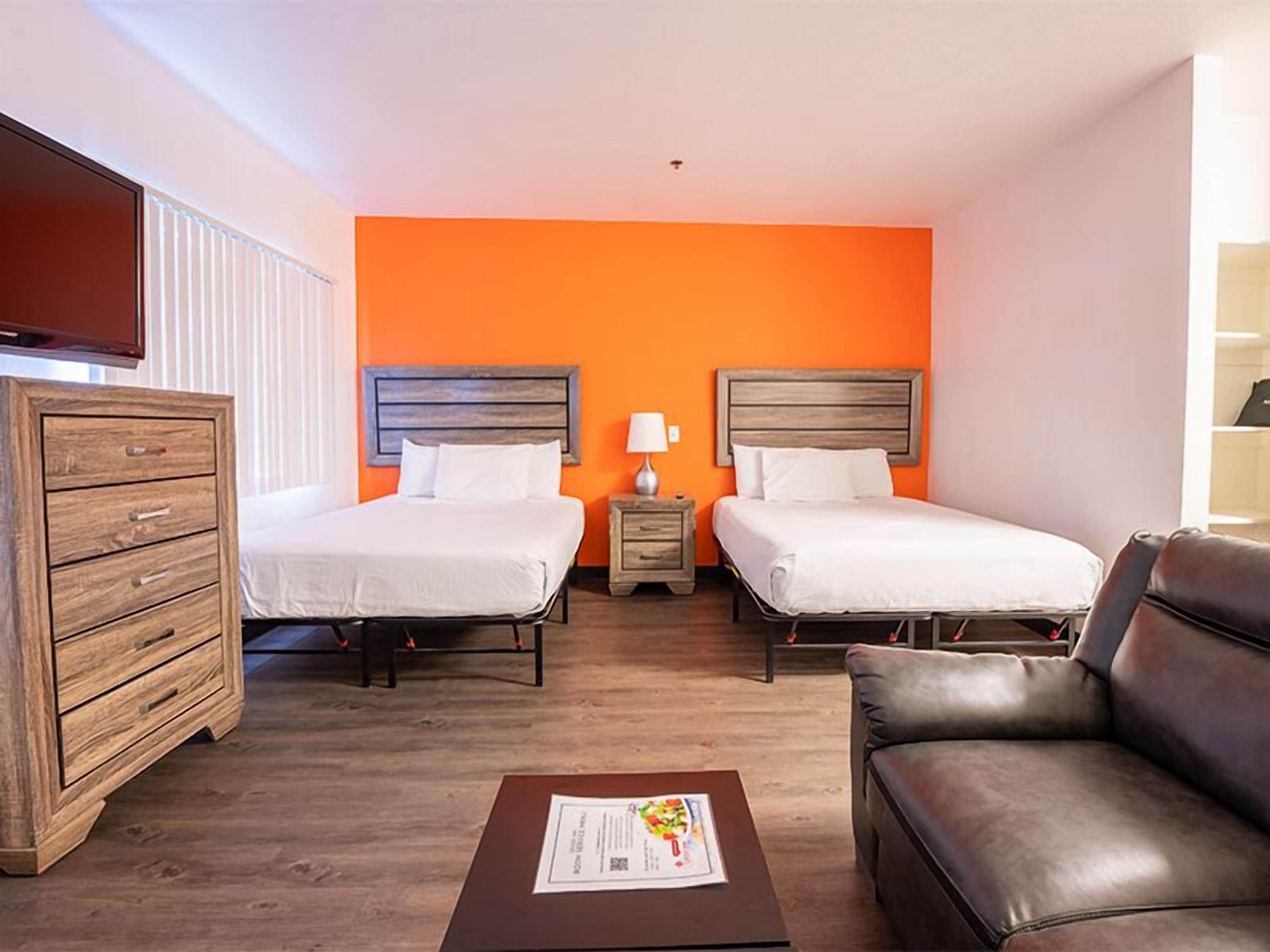 Ein Hotelzimmer mit zwei Betten, einem Holzkasten, einem Ledersofa und einem Flachbildfernseher.