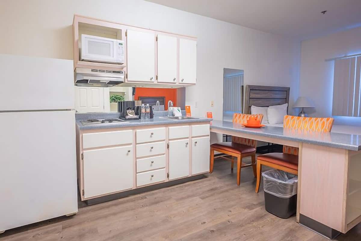 A modern kitchen with white cabinets, a microwave, and a coffee machine. There is a small dining area with a table and chairs.