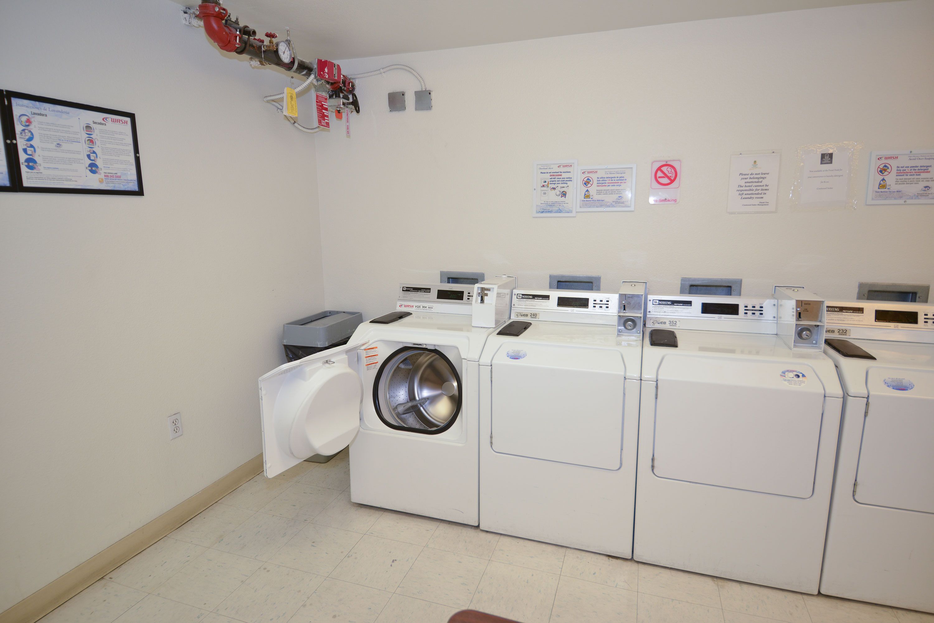 Une buanderie équipée de plusieurs machines à laver et de plusieurs sèche-linge, d’un extincteur et de panneaux de signalisation de sécurité fixés au mur.