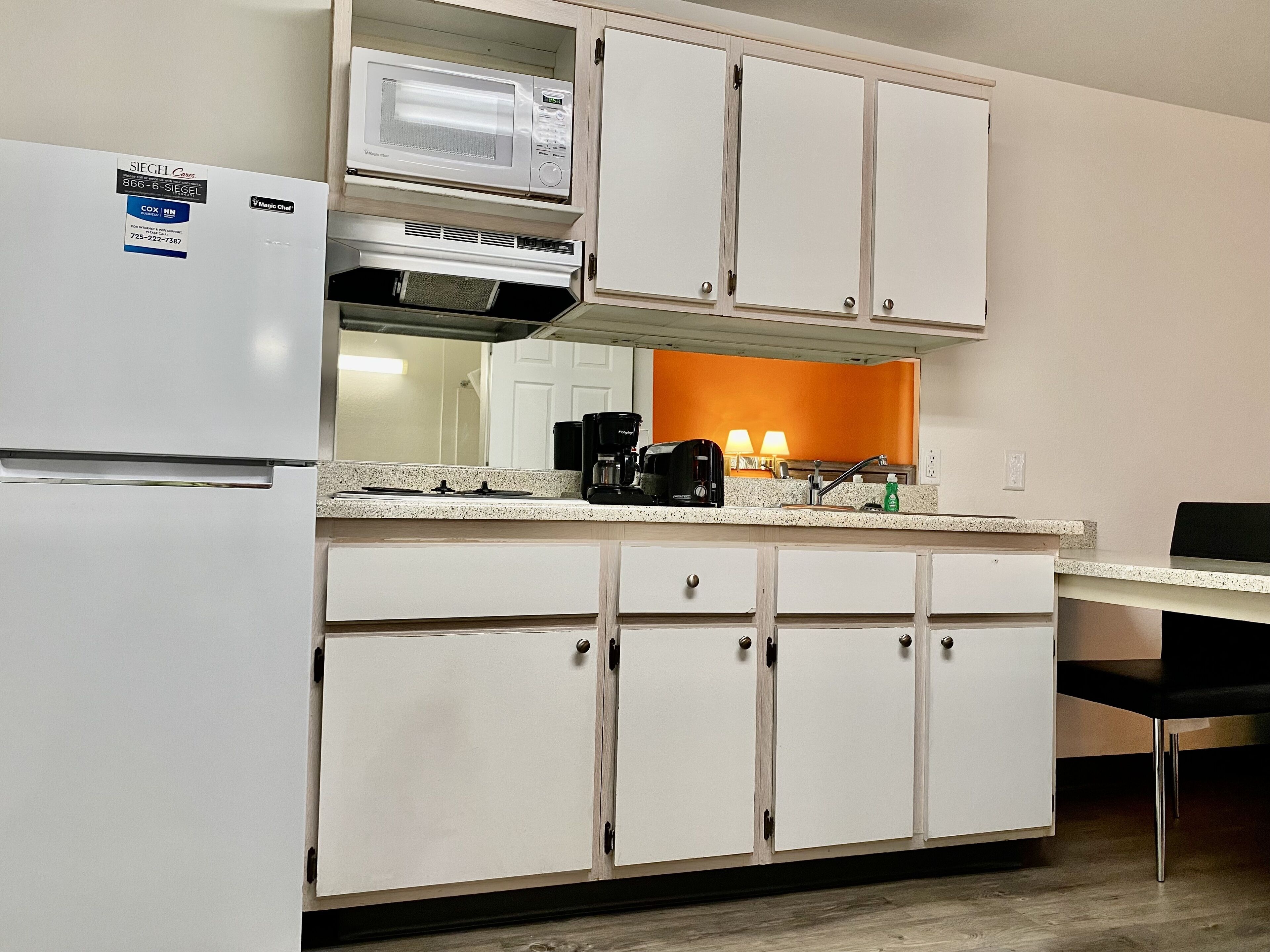 A compact kitchen with white cabinets, a microwave, a coffee maker, and a sink.