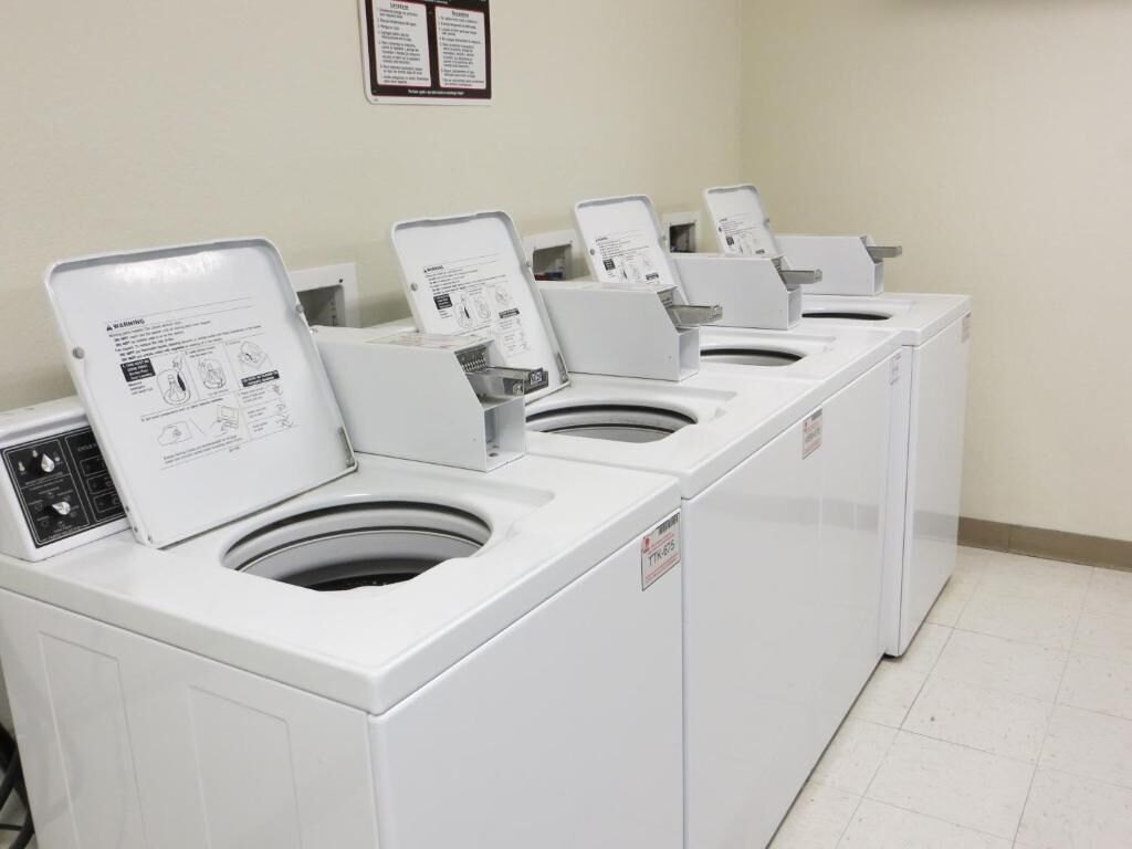 Een rij witte wasmachines met voorlaadklep in een openbare wasserette, met instructieborden op elke machine.