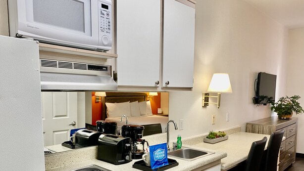 Cocina compacta con microondas, cafetera y tostadora. Hay un lavamanos con grifo, una pequeña zona de encimera y una mesa de comedor con sillas.