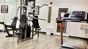Un gimnasio con equipo de ejercicio, una cinta de correr y una pared con ilustraciones de ejercicios.