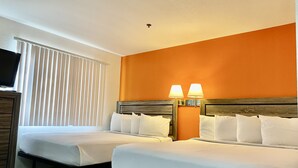 Habitación de hotel con dos camas, ropa de cama blanca, una pared de acento naranja y dos lámparas de noche.