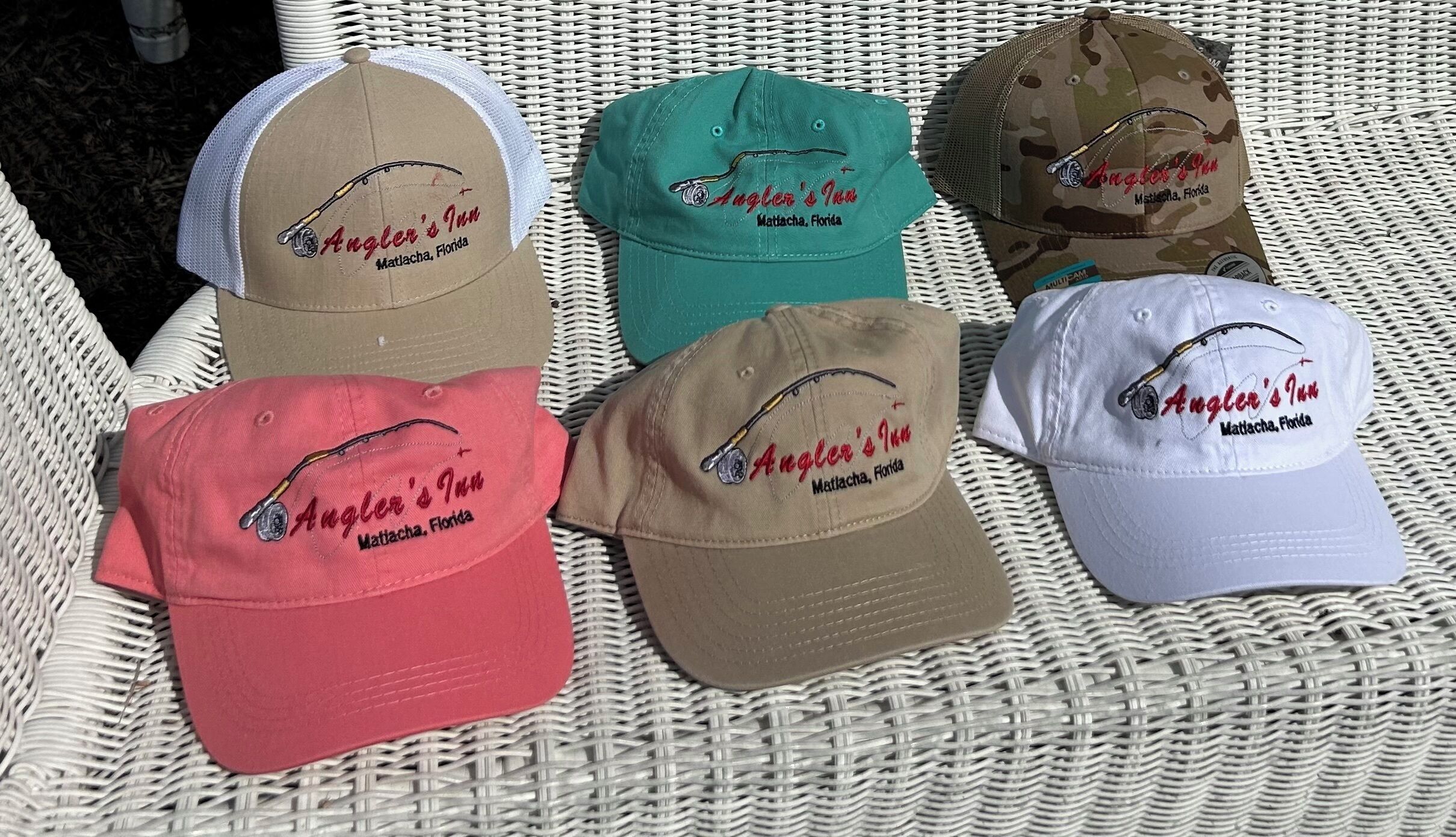 Six caps with embroidered text and a fishing hook design, placed on a woven surface.