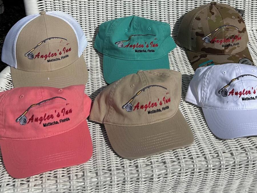 Six caps with embroidered text and a fishing hook design, placed on a woven surface.
