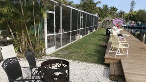 A patio area with outdoor seating, a grill, and a view of a building with large windows. - Angler's Inn (Matlacha)