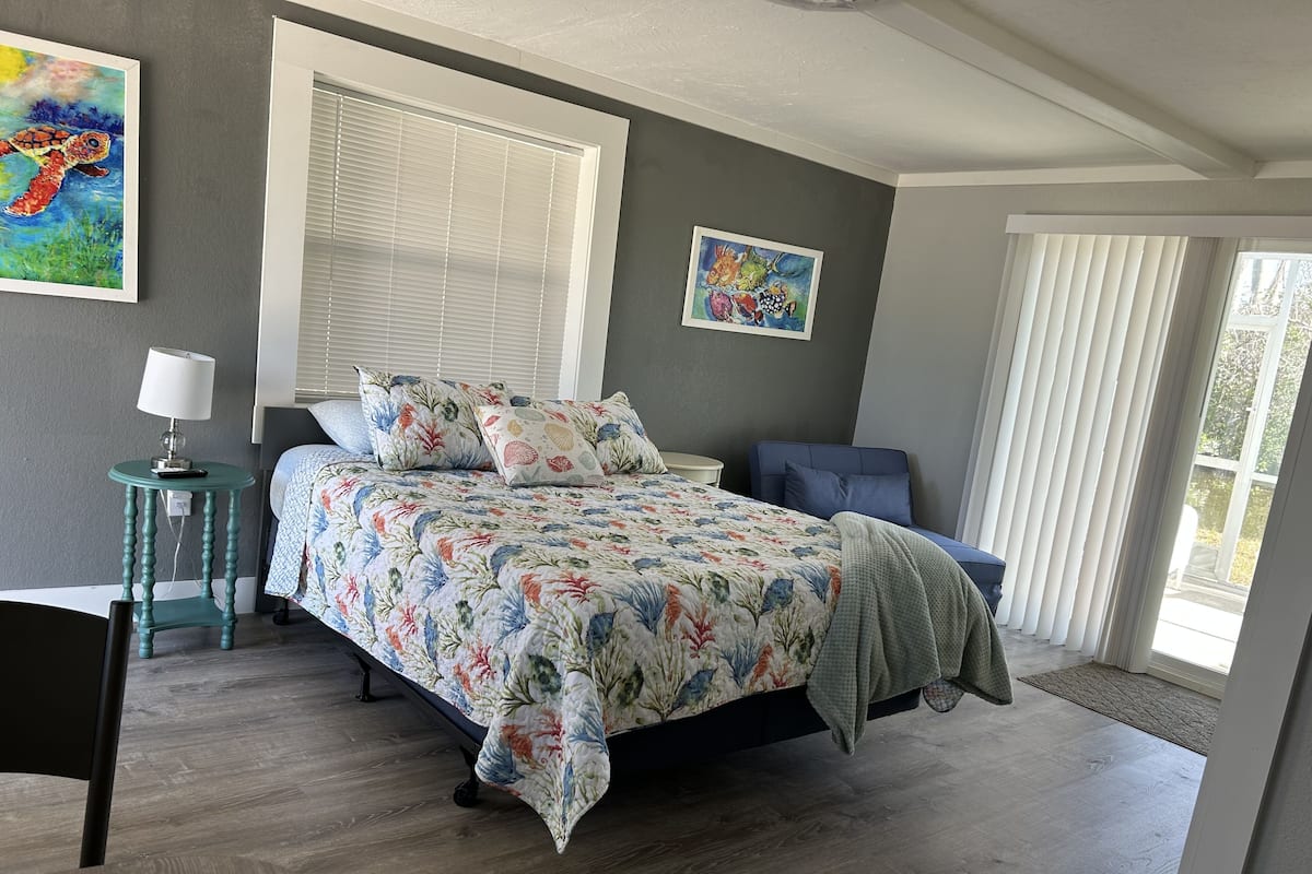 A bedroom with a bed, a desk, a chair, a lamp, and two paintings on the wall.