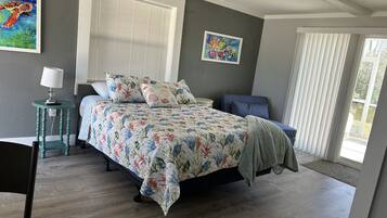 A bedroom with a bed, a desk, a chair, a lamp, and two paintings on the wall.