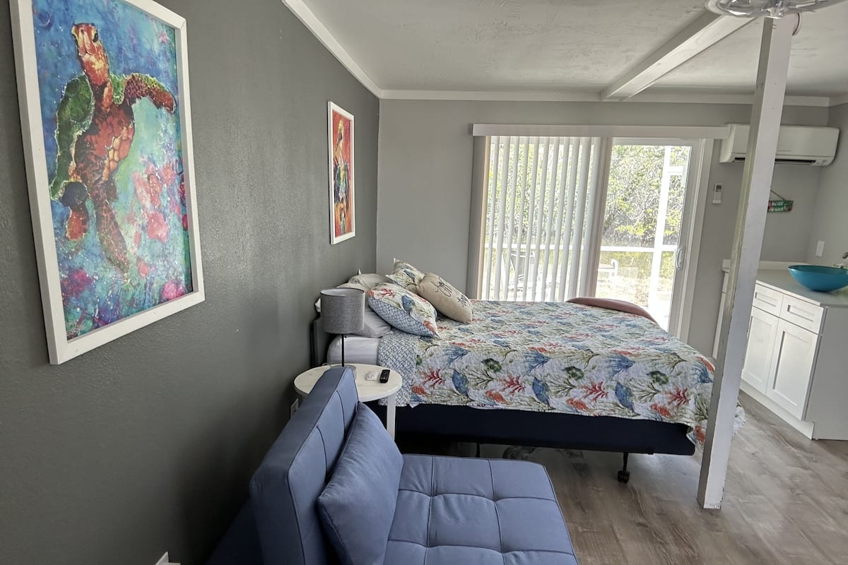 A bedroom with a bed, a bedside table, a lamp, a chair, and a painting on the wall.