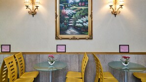 A room with a framed painting, two wall-mounted lamps, and three glass tables with yellow chairs. - Flushing Hotel (Flushing)