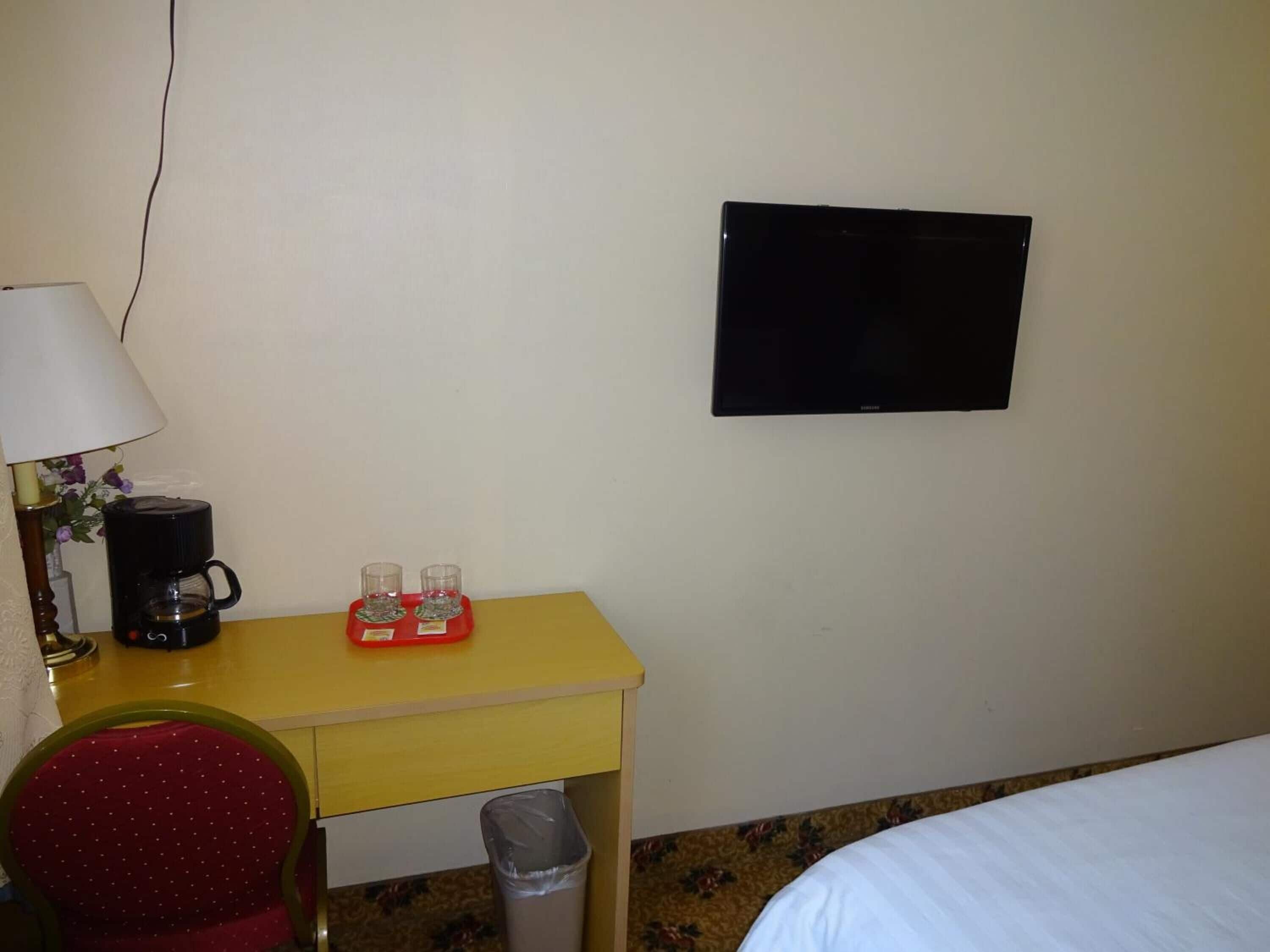 Une chambre d’hôtel avec un lit, un bureau doté d’une lampe, une machine à café et deux verres posés sur le bureau.