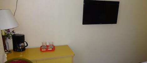 Une chambre d’hôtel avec un lit, un bureau doté d’une lampe, une machine à café et deux verres posés sur le bureau.