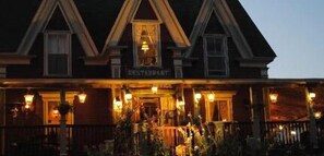 A traditional building with a sign reading "RESTAURANT" at the entrance, featuring a porch with outdoor seating and decorative lighting.