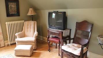 Una sala de estar con televisor sobre un mueble, un radiador, una lámpara y dos sillones.