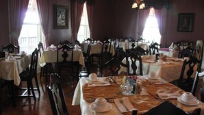 A dining area with multiple tables set for service, each with white tablecloths and silverware. - Lynwood Inn (Baddeck)