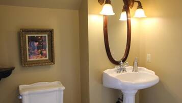 A bathroom with a white pedestal sink, a large mirror with a wooden frame, and a framed picture on the wall.