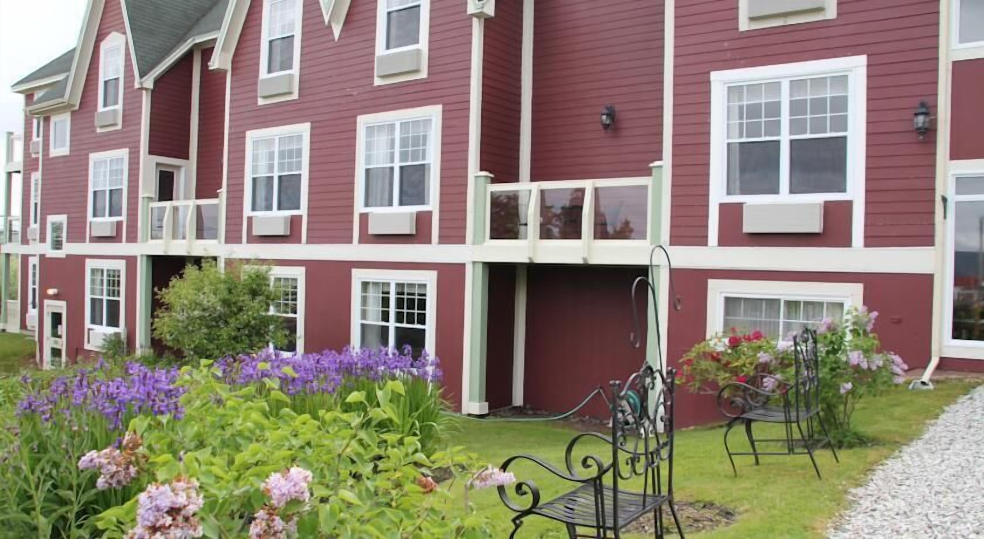 A red building with multiple windows and a garden with flowers and benches.