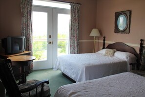 A hotel room with two beds, a television on a wooden table, and a balcony with curtains.