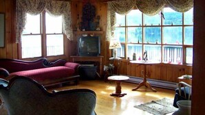 A cozy cabin interior with a wooden ceiling, a fireplace, a television, a sofa, and a dining table. - Lynwood Inn (Baddeck)