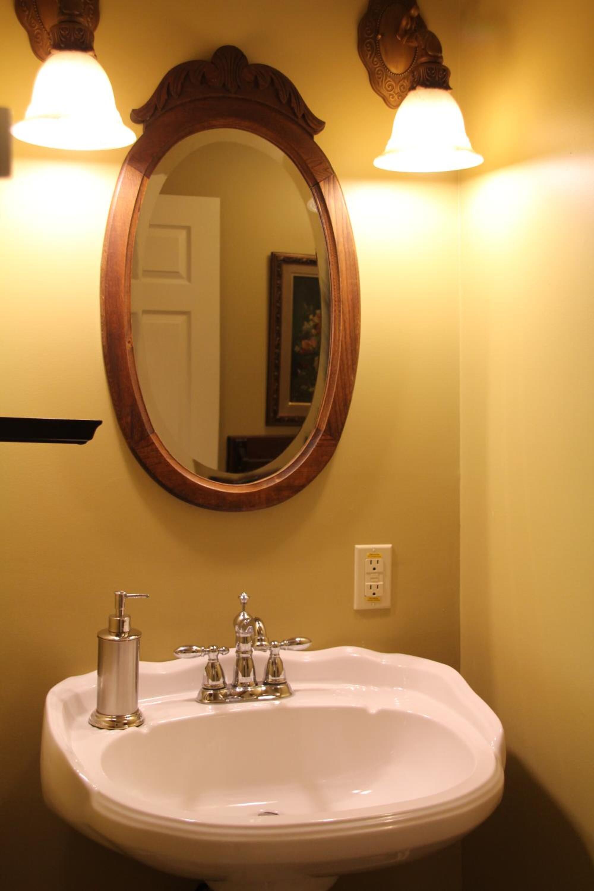Un baño con un lavamanos blanco, dos luces empotradas en la pared y un espejo con marco de madera.