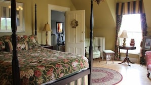 A bedroom with a four-poster bed, a chair, a small table, and a window with curtains. - Lynwood Inn (Baddeck)