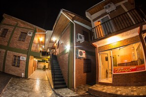 A building with a staircase leading to a second floor, a door with a sign reading "Lo de Carmen Apart," and air conditioning units mounted on the exterior walls.