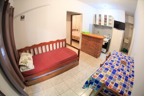 Habitación compacta con una cama individual, un pequeño rincón americano y un baño a la vista a través de una puerta abierta.