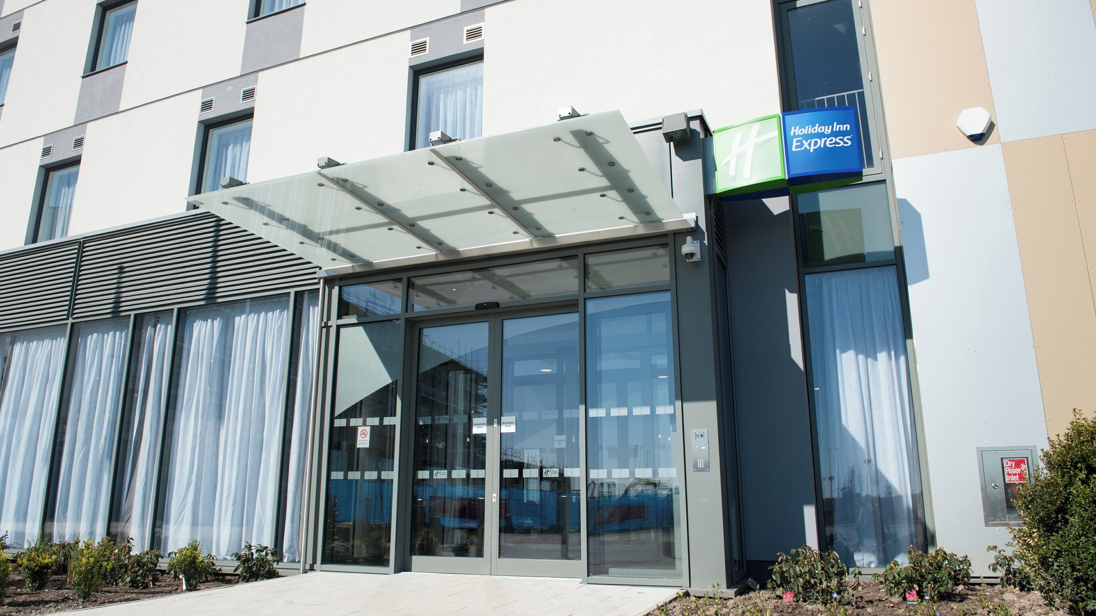 Edificio de Holiday Inn Express con una entrada de vidrio moderna, un paseo techado y un cartel.