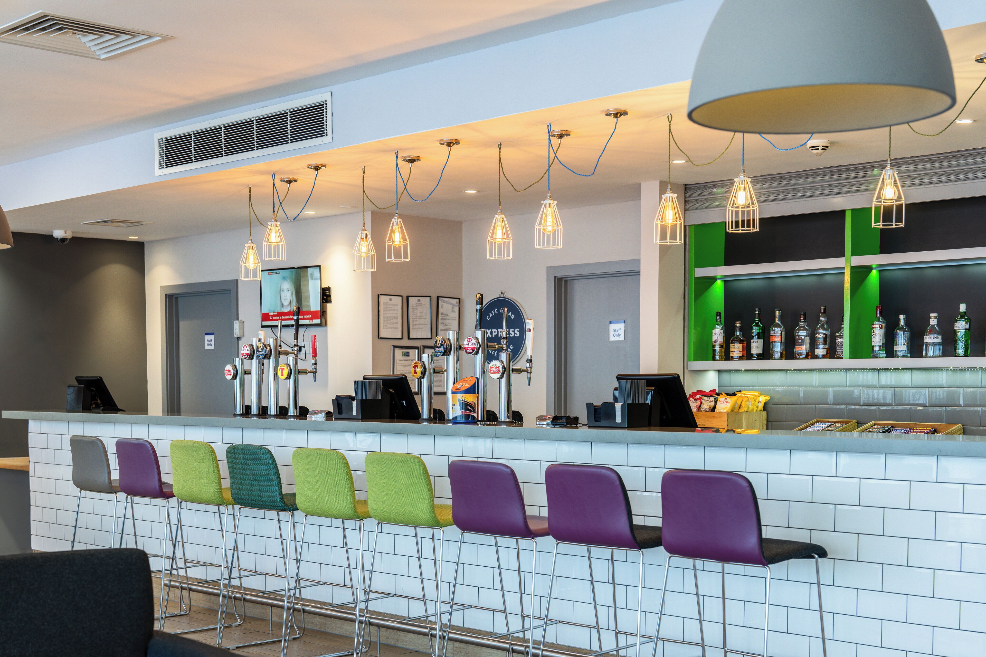 A bar area with a white tiled counter, colorful bar stools, and a variety of liquor bottles.