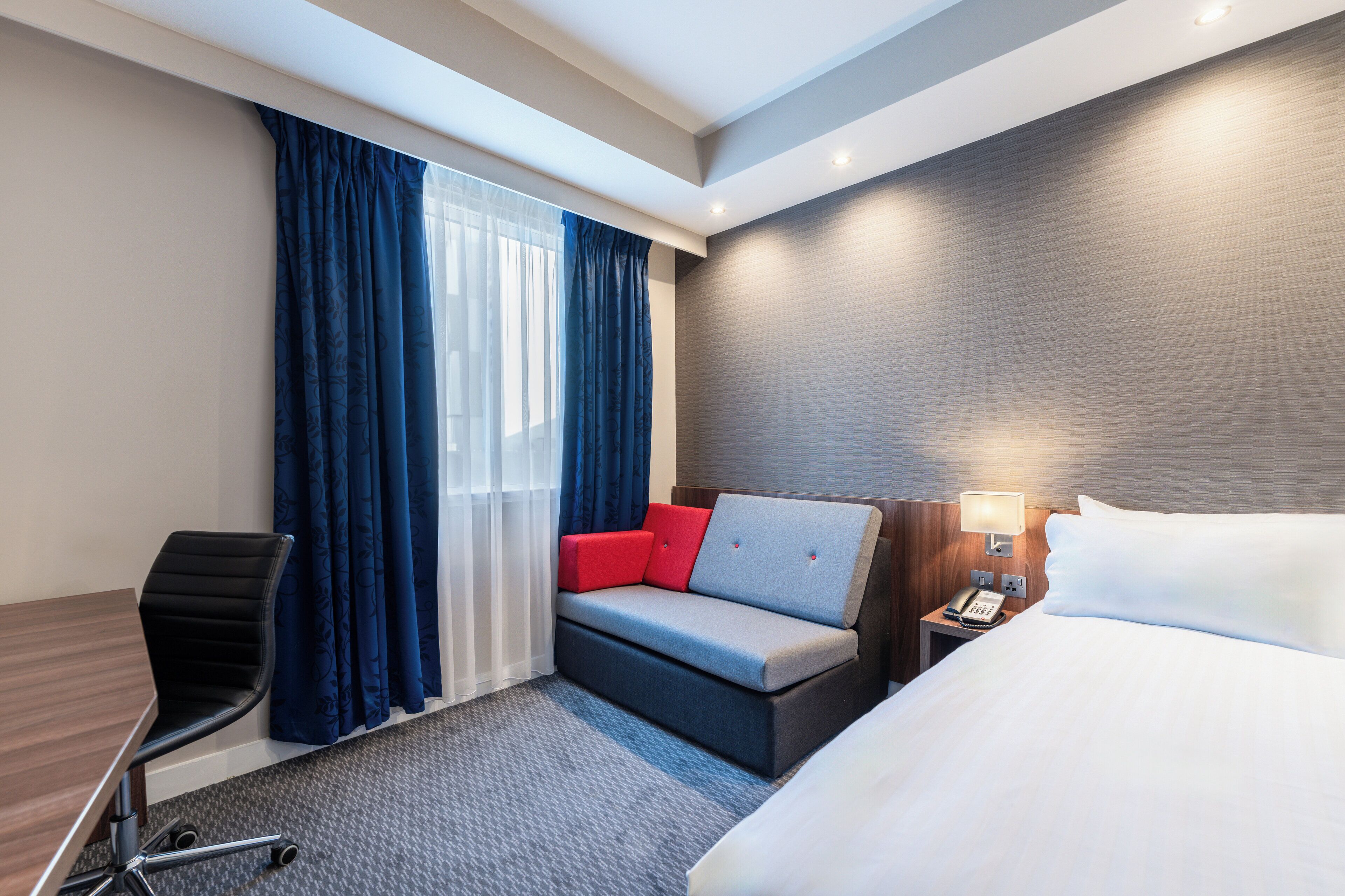 Una habitación de hotel con cama, sofá con cojines rojos, escritorio y silla.