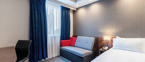 Una habitación de hotel con cama, sofá con cojines rojos, escritorio y silla.
