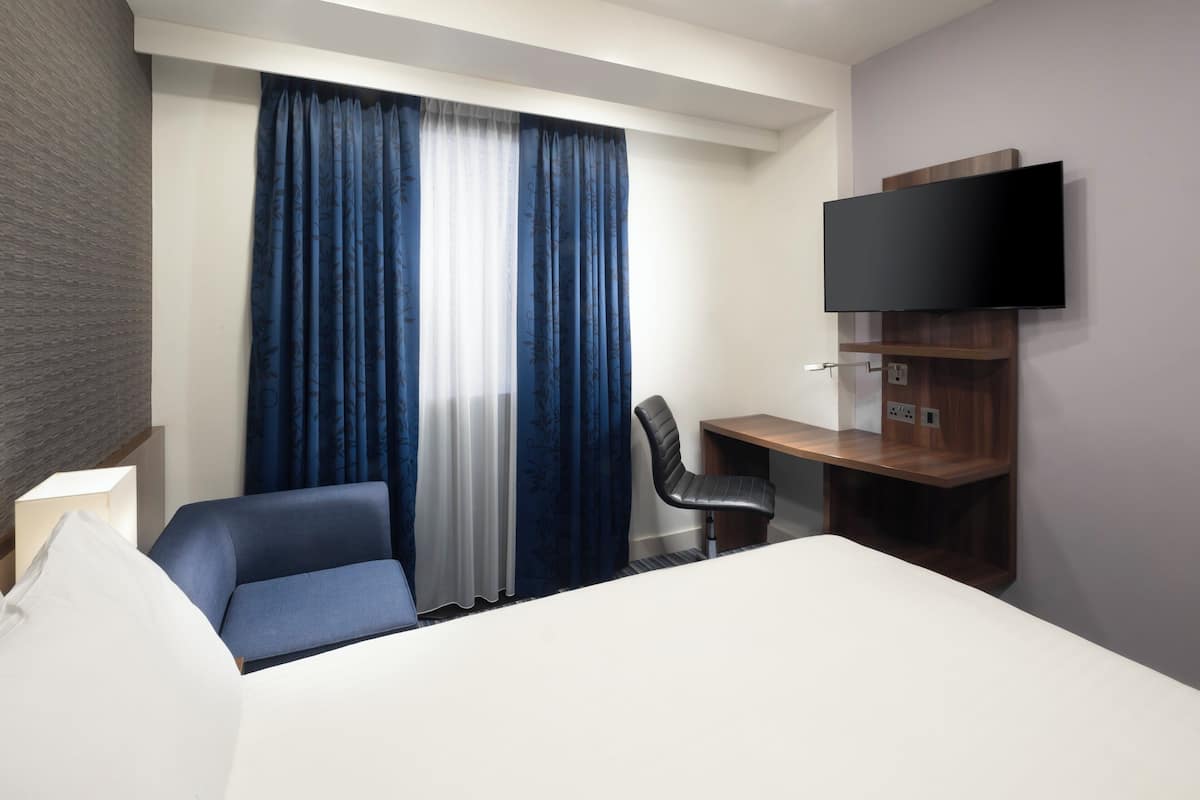 A hotel room with a bed, a desk, a chair, a television, and a window with curtains.