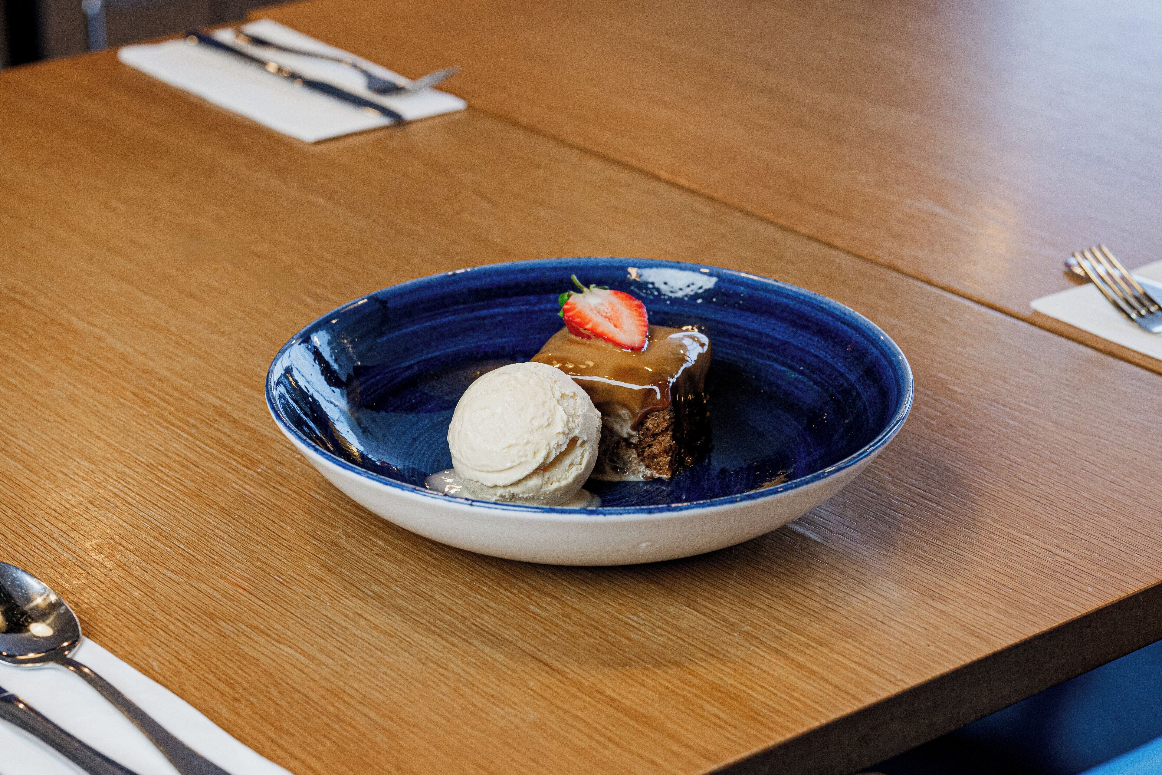 A dessert plate with ice cream and a piece of cake on a wooden table.