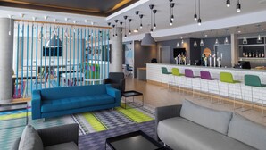 Un espace lounge moderne avec un canapé bleu, un canapé gris et des fauteuils colorés, un bar avec un comptoir et un coin salon agrémenté d’un tapis à motifs.