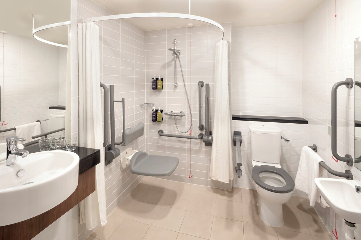 A modern bathroom with a shower, toilet, sink, and grab bars.