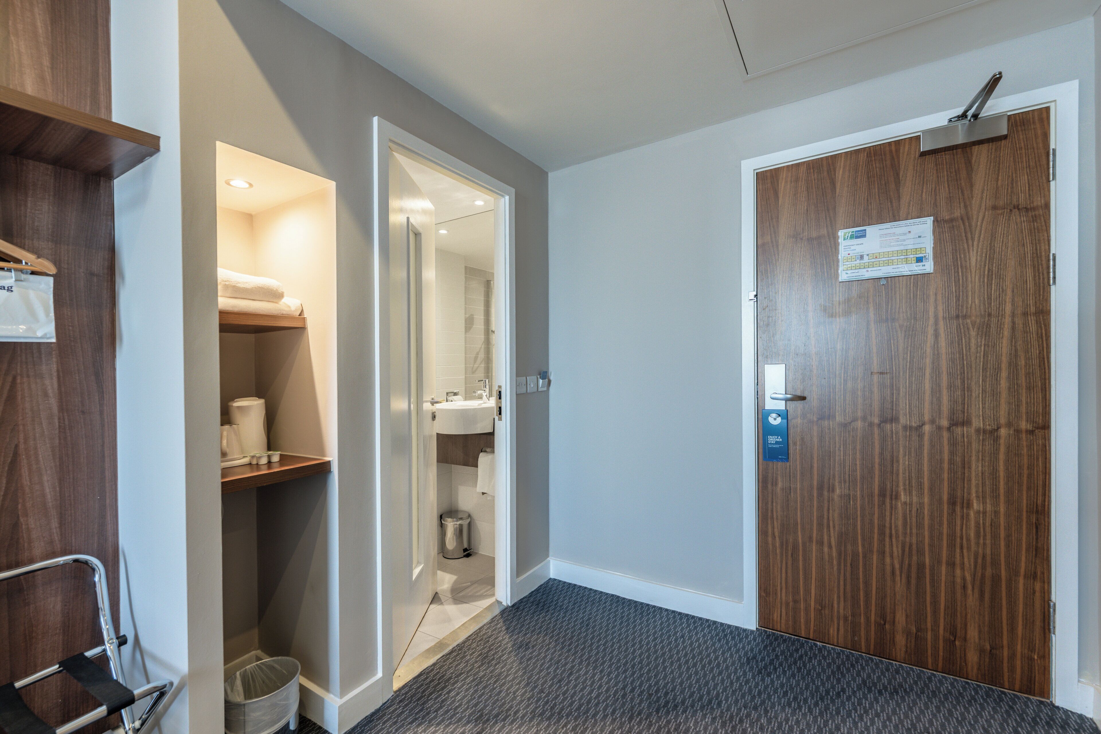 A hotel room with a wooden door, a small bathroom with a sink and toilet, and a shelf with towels.