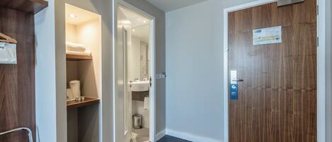 A hotel room with a wooden door, a small bathroom with a sink and toilet, and a shelf with towels.