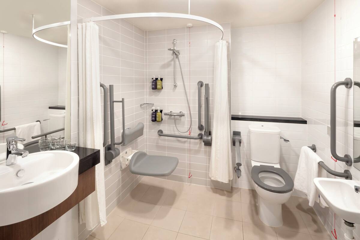 A modern bathroom with a shower, toilet, sink, and grab bars.