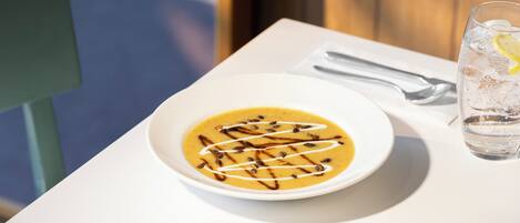 A white table with a bowl of soup, a glass of water, a small plate with butter, and a piece of bread.