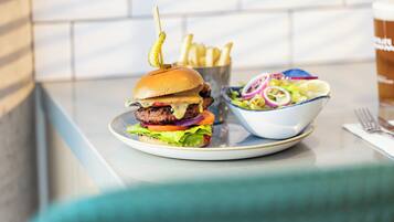 Hamburguesa con papas fritas y ensalada en un plato, y una bebida al fondo.