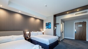 Une chambre d’hôtel avec deux lits, un grand tableau, une porte en bois et une table de chevet avec un téléphone.
