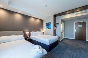 Habitación de hotel con dos camas, un cuadro grande, una puerta de madera y una mesita de noche con un teléfono.