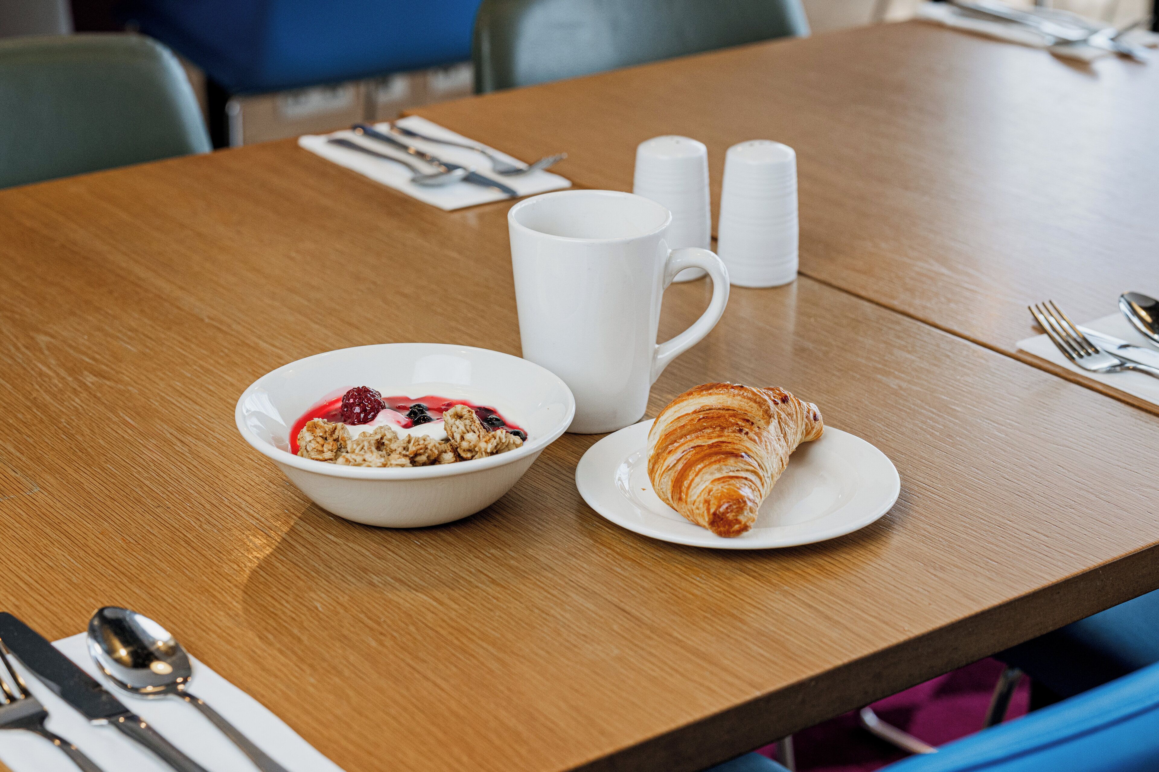 A breakfast setting with a bowl of cereal and a croissant on a wooden table.