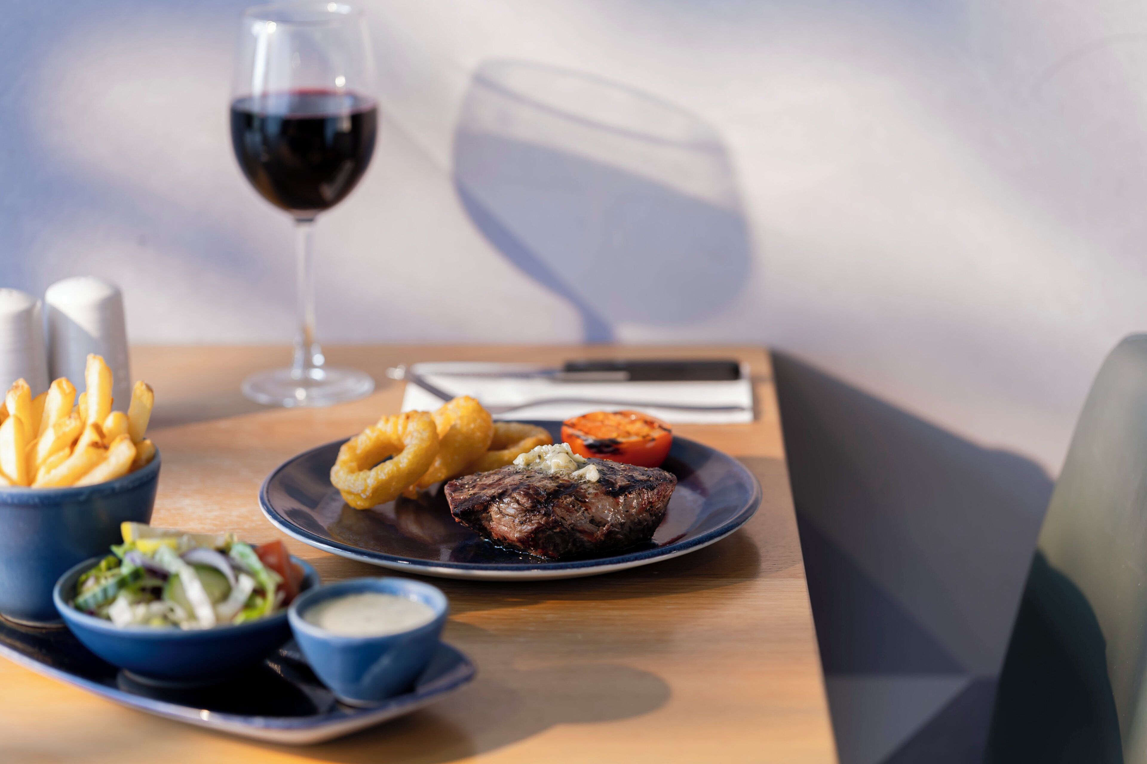 Un plato con bistec, papas fritas y una copa de vino tinto sobre una mesa de madera.