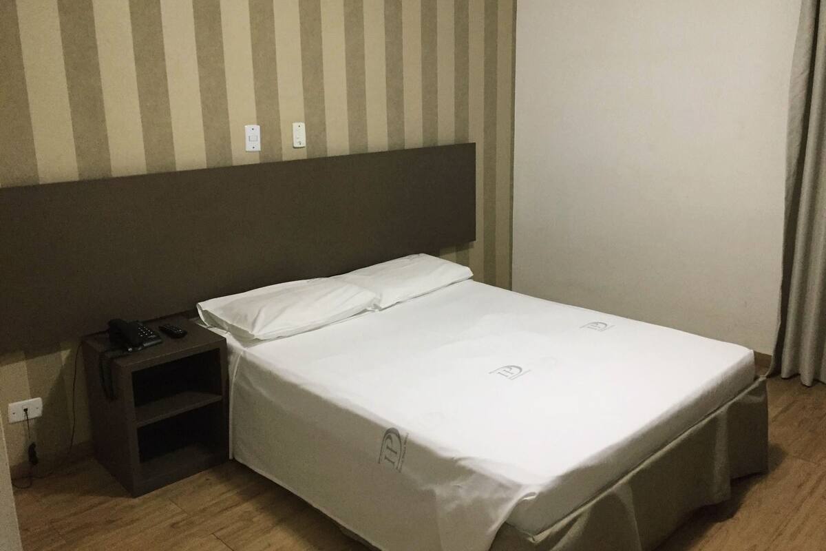 Ein Hotelzimmer mit einem Einzelbett, einem Nachttisch und einem an der Wand befestigten Fernseher.