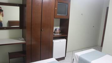 Une petite pièce, de taille modeste, comprenant une armoire en bois, un petit réfrigérateur, une télévision et deux lits avec des couvre-lits assortis.
